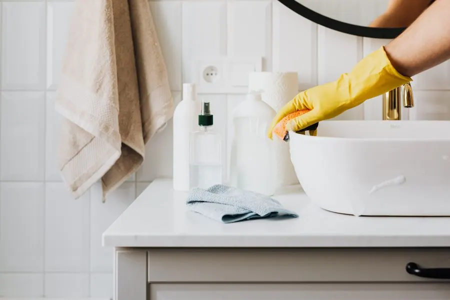Scrubbing a bathroom sink in gloves during a deep cleaning in Metro Detroit